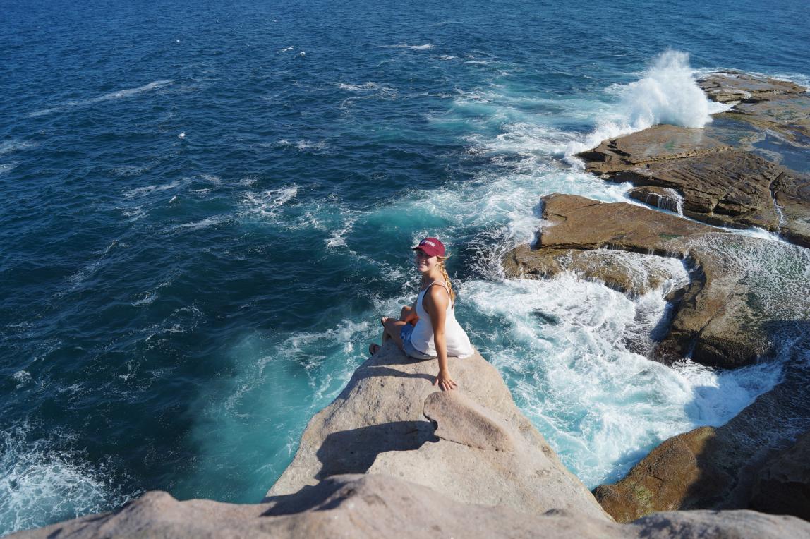 a student poses for a photo on a seaside rock in Sydney