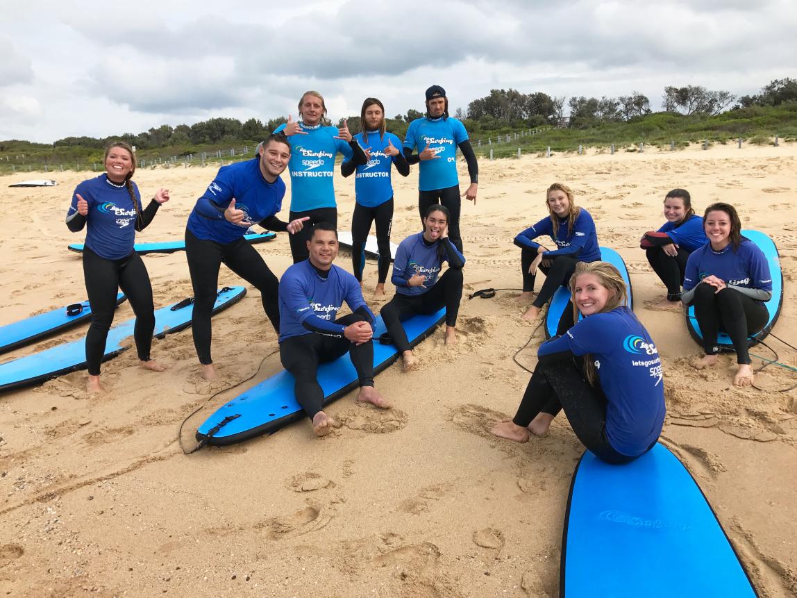 a group of students pose for a photo with their surf boards and surf gear on the beach in Sydney